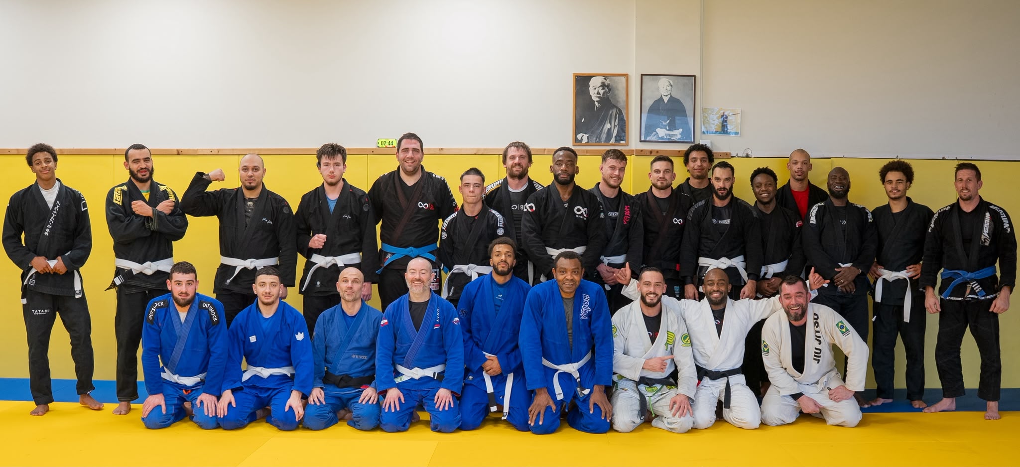 Photo de groupe des pratiquants en kimono devant le mur jaune du dojo de Pierrelaye