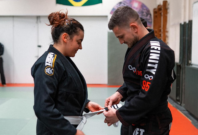 Coach nouant une ceinture blanche à une pratiquante au dojo